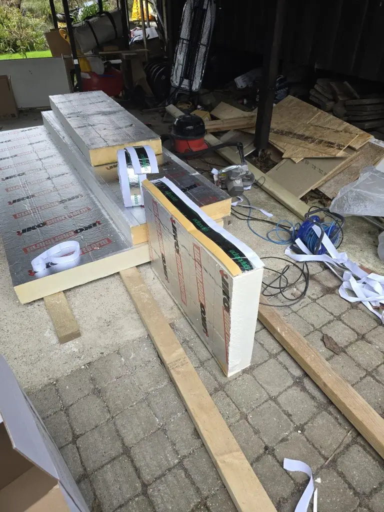 PIR insulation boards being cut on a workbench outside, with tools and tape around.