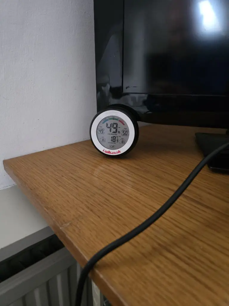 A small digital thermometer on a desk, logging the room temperature.