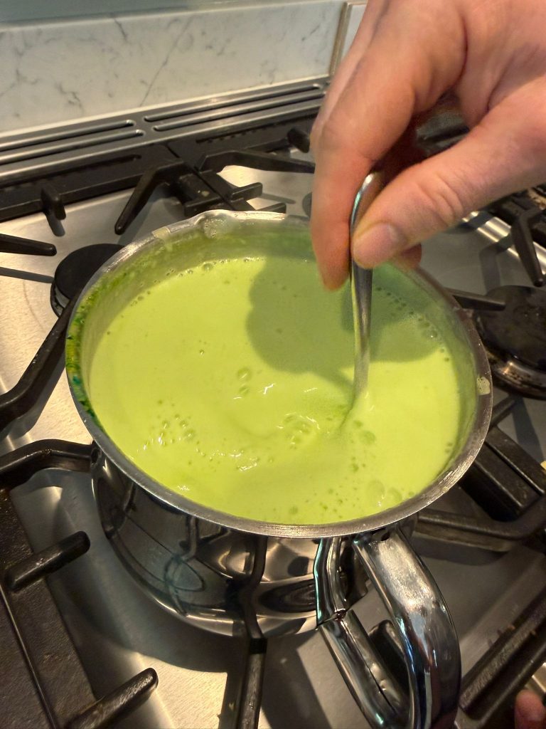 Bright green mint custard base simmering in a saucepan, stirred with a spoon