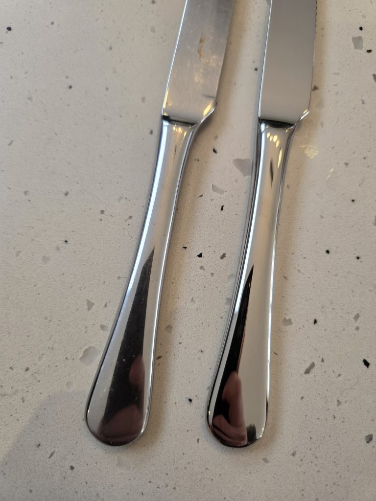 An older Robert Welch Radford table knife beside a new one, on a speckled worktop.