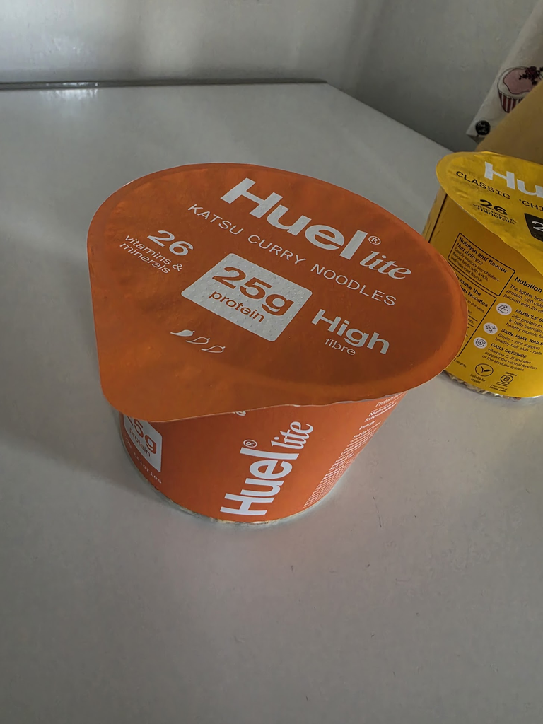 An orange Huel Lite Hot & Savoury pot on a table.